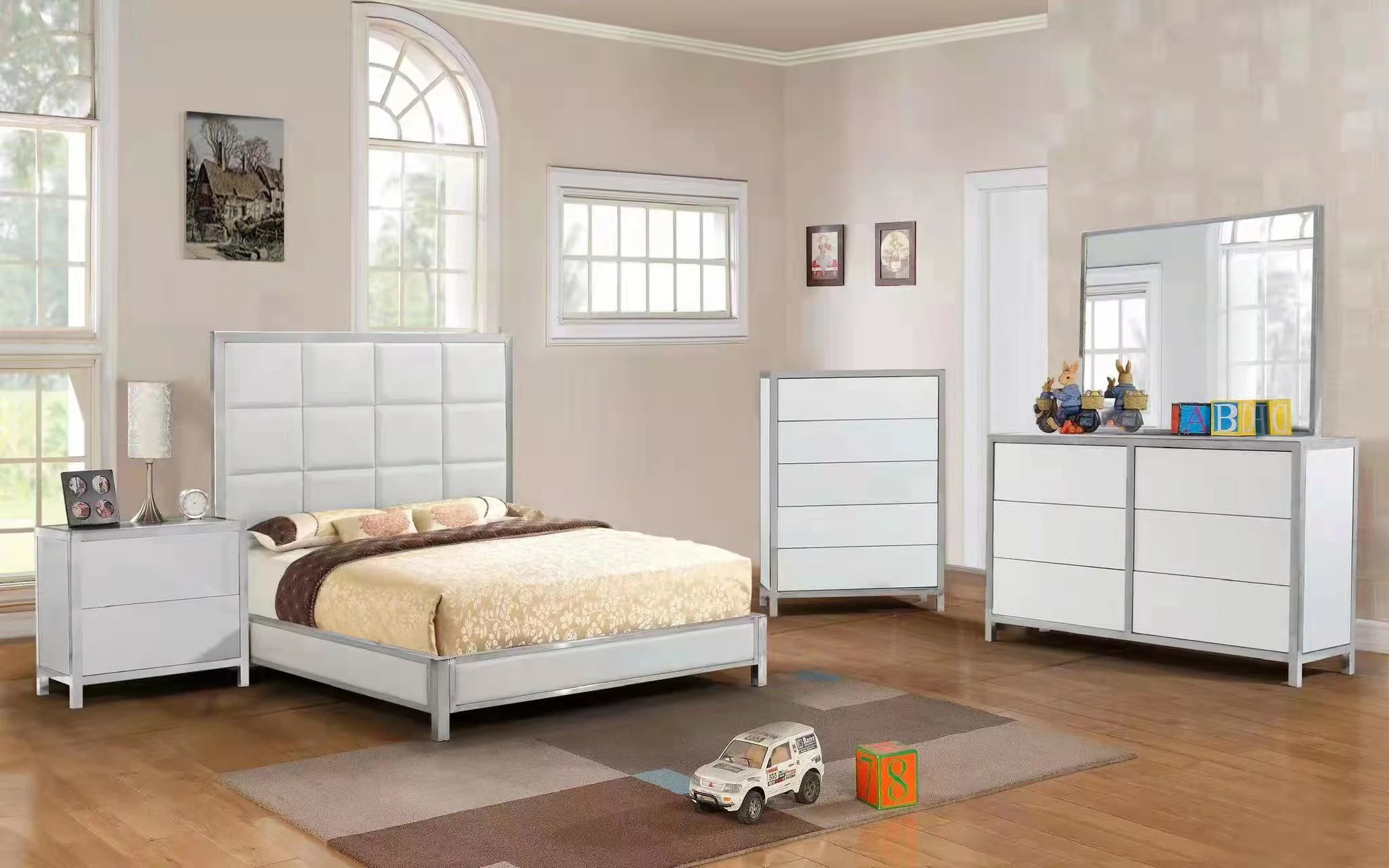 White bed, bedside cabinet, tall chest and mirrored dresser in a bright bedroom.